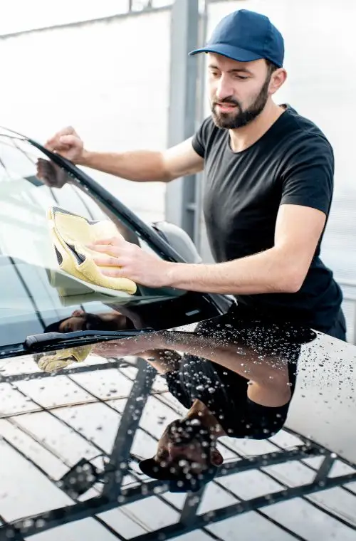 man wearing cap wiping the car windshield