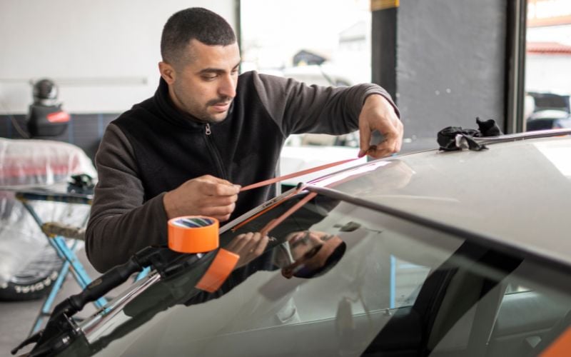 the man is adding a tape-in the car windshield