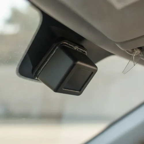 Close-up of a black ADAS camera housing mounted at the top interior of a vehicle windshield near the mirror base.